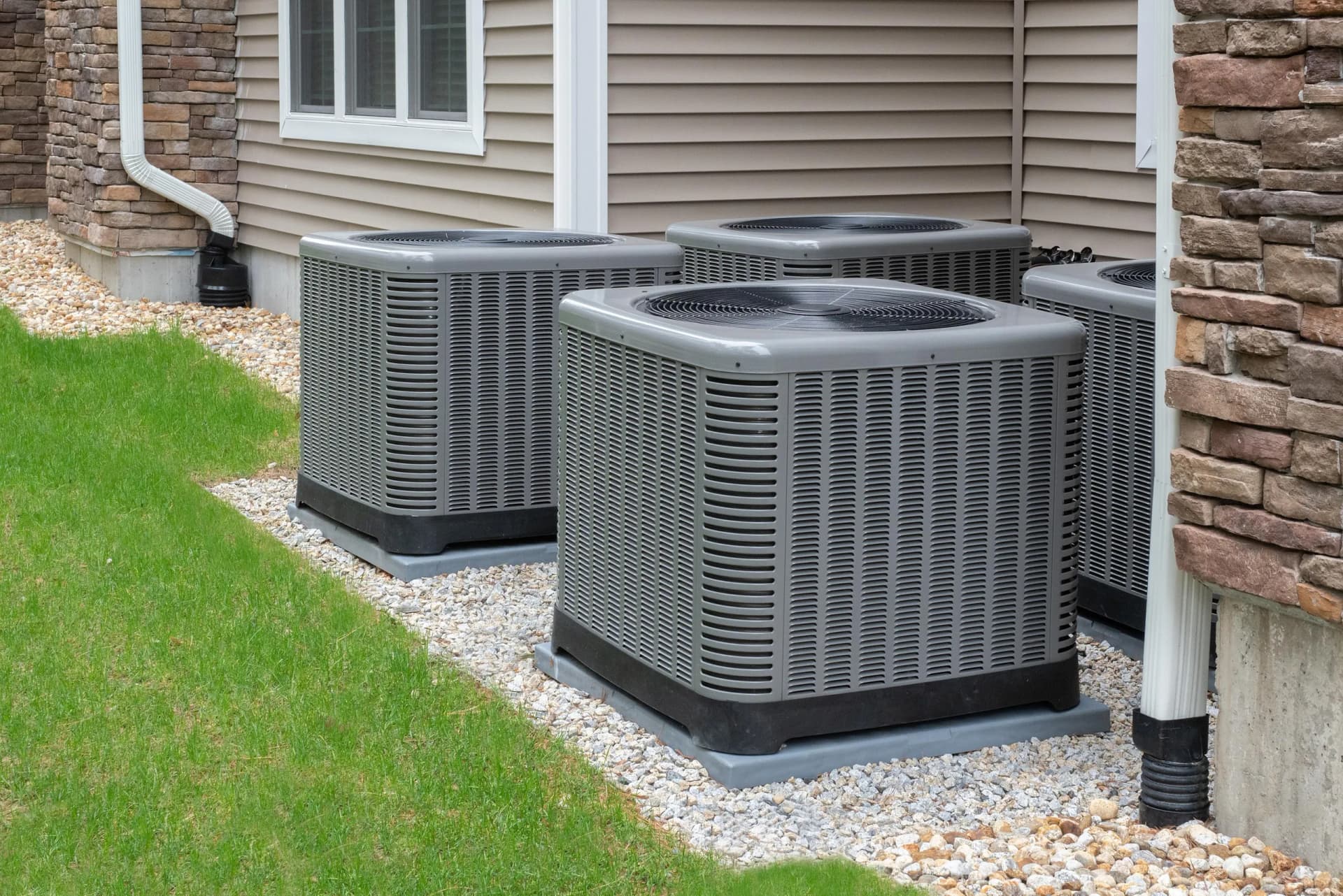 Multiple outdoor air conditioning or HVAC units installed next to the exterior of a modern residential building with siding and stone.