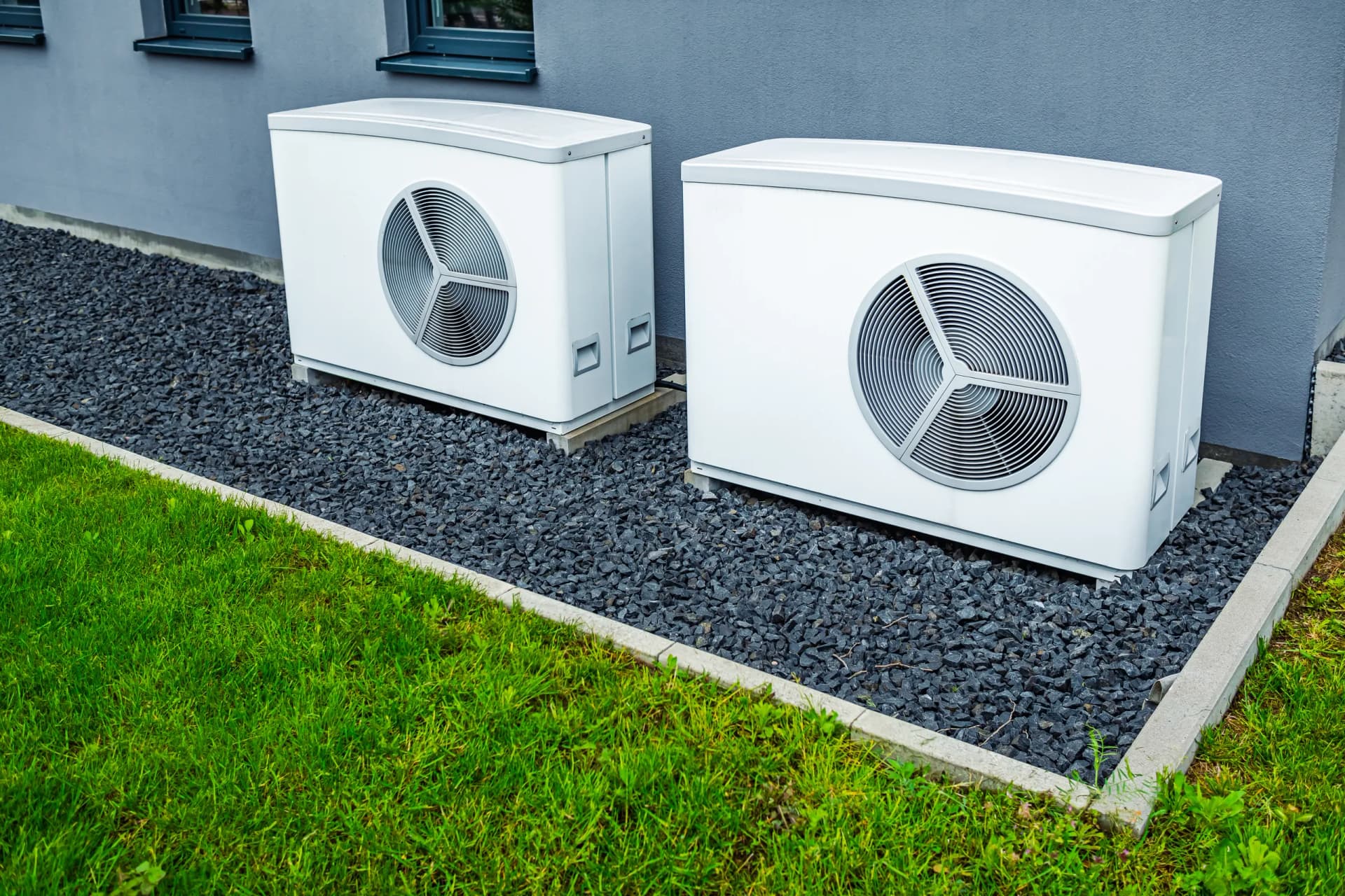 Outdoor heat pump condenser unit on concrete pad beside home with refrigerant lines